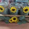 Sunflowers attached to three mason jars that are painted green in a wooden box